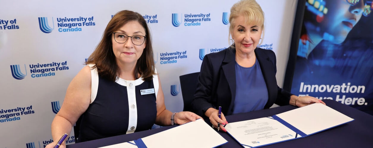 Two women engaged in signing documents at a table, set against a blue background