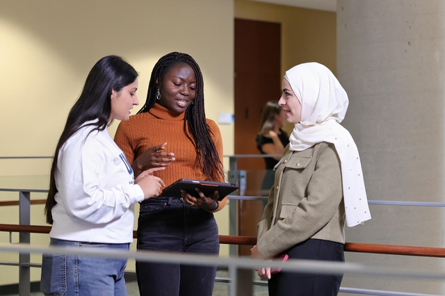A group of three individuals with an ipad engaged in a conversation