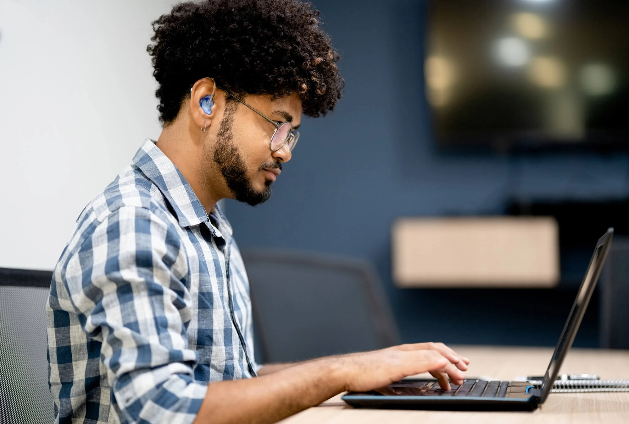 A guy with an earphones typing on a laptop
