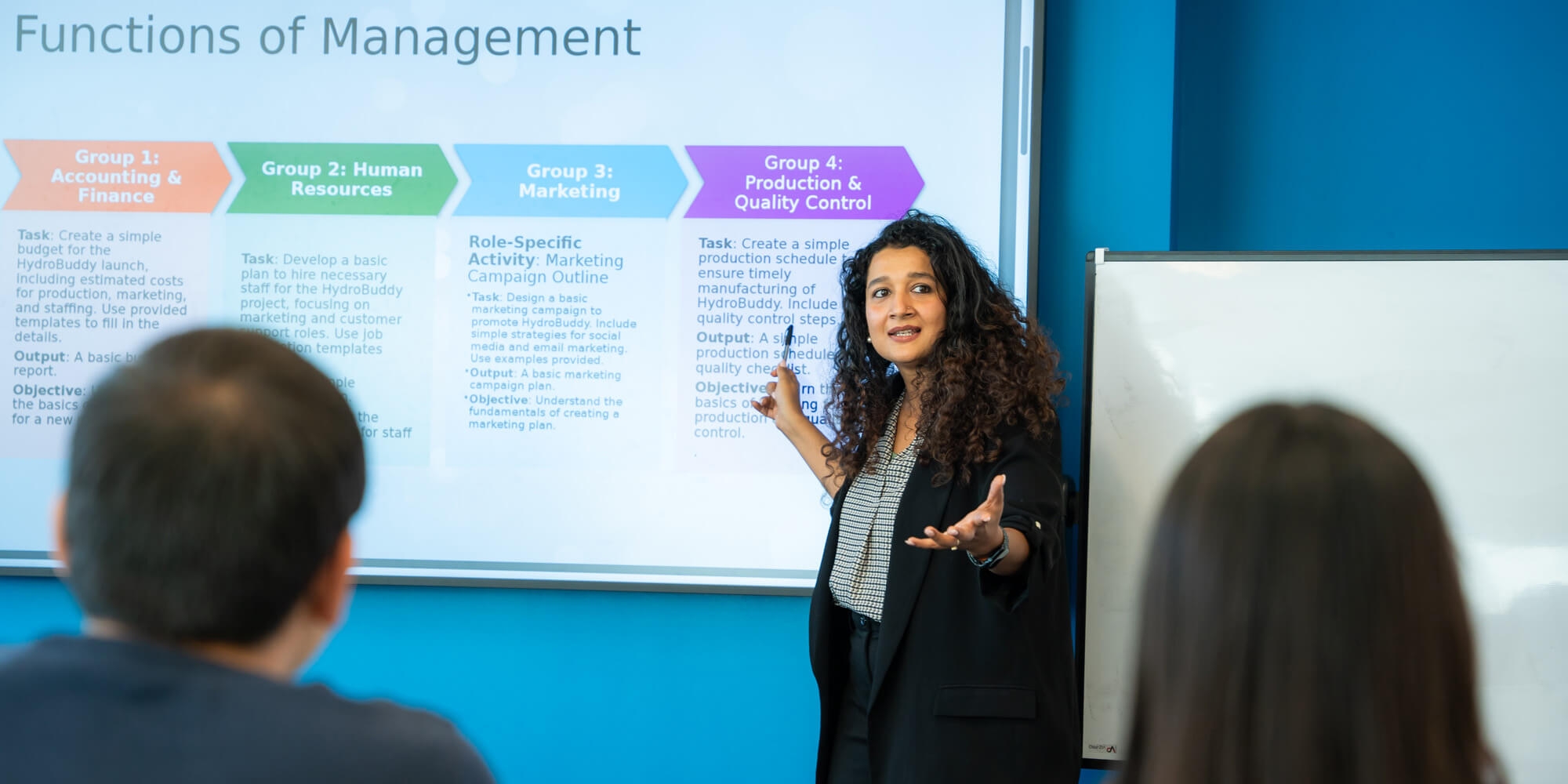 A woman stands confidently at the front, presenting to an engaged audience of diverse individuals seated in a conference room