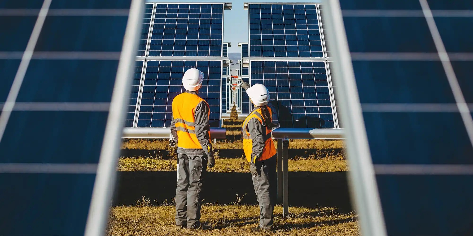 two workers wearing safety helmets and working on solar panels