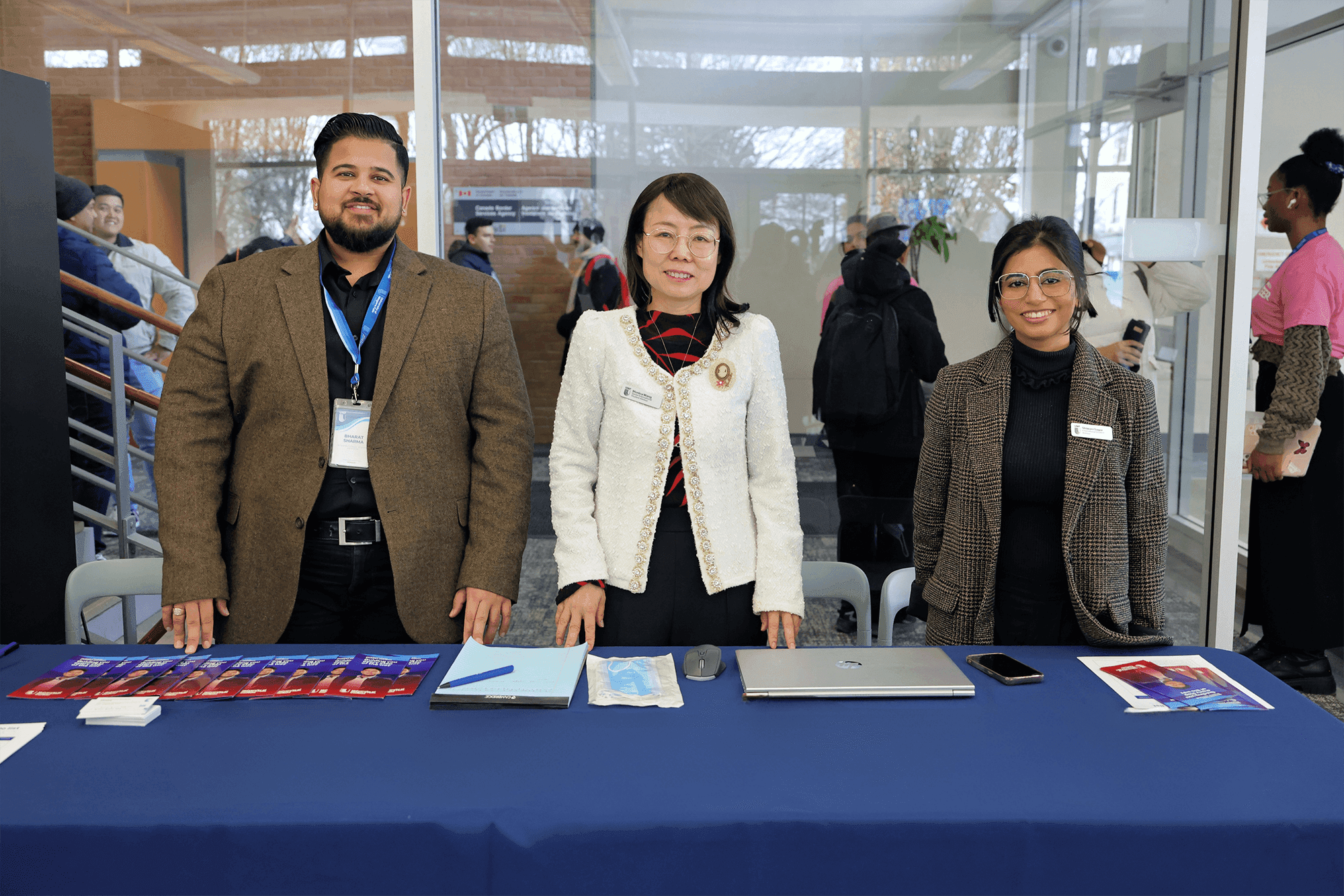 Three individuals stand behind a table, each using a laptop, engaged in a collaborative work environment