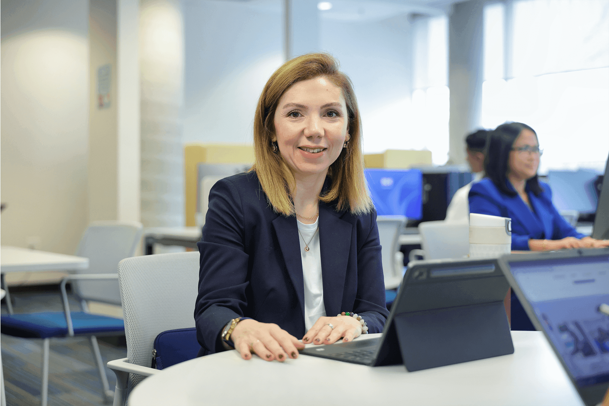 A woman sitting in front of a tablet and smiling for the camera