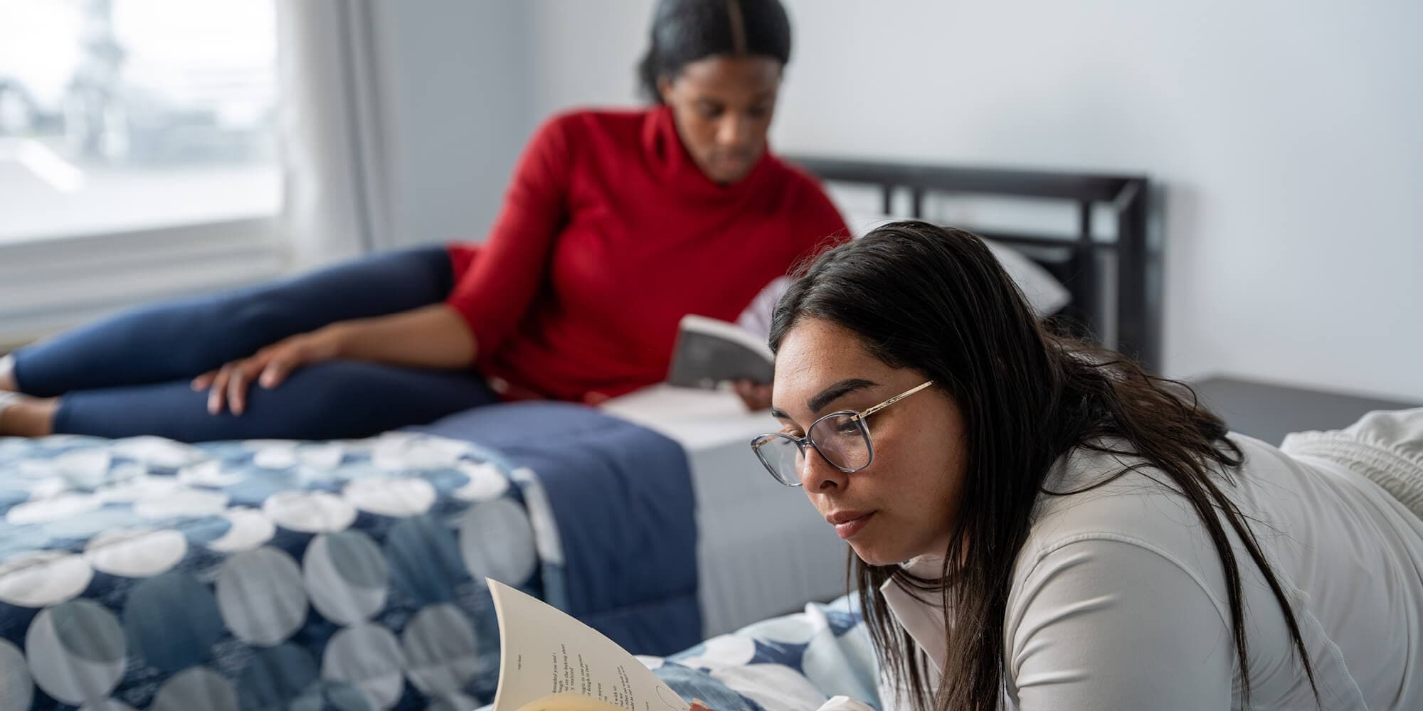 A group of two women sits on their beds, engrossed in reading a book, surrounded by a cozy atmosphere
