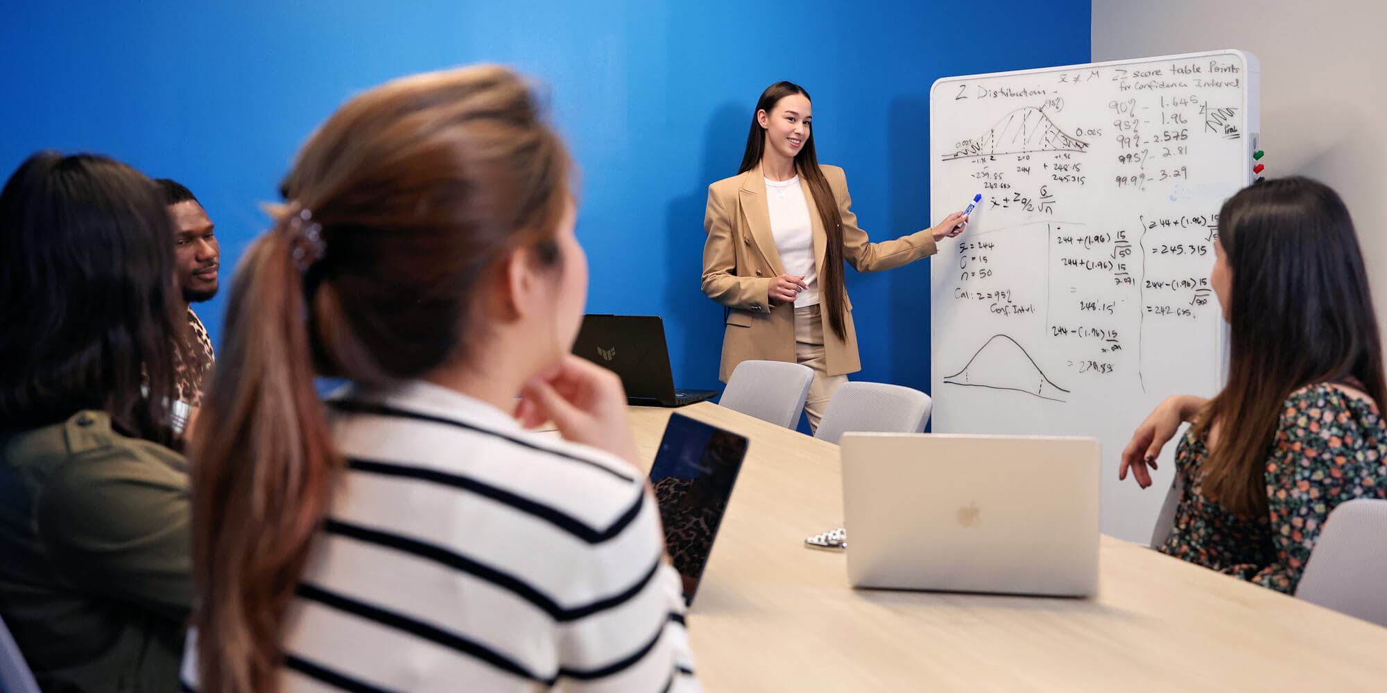 A woman stands before a group, confidently presenting her topic while the audience listens attentively