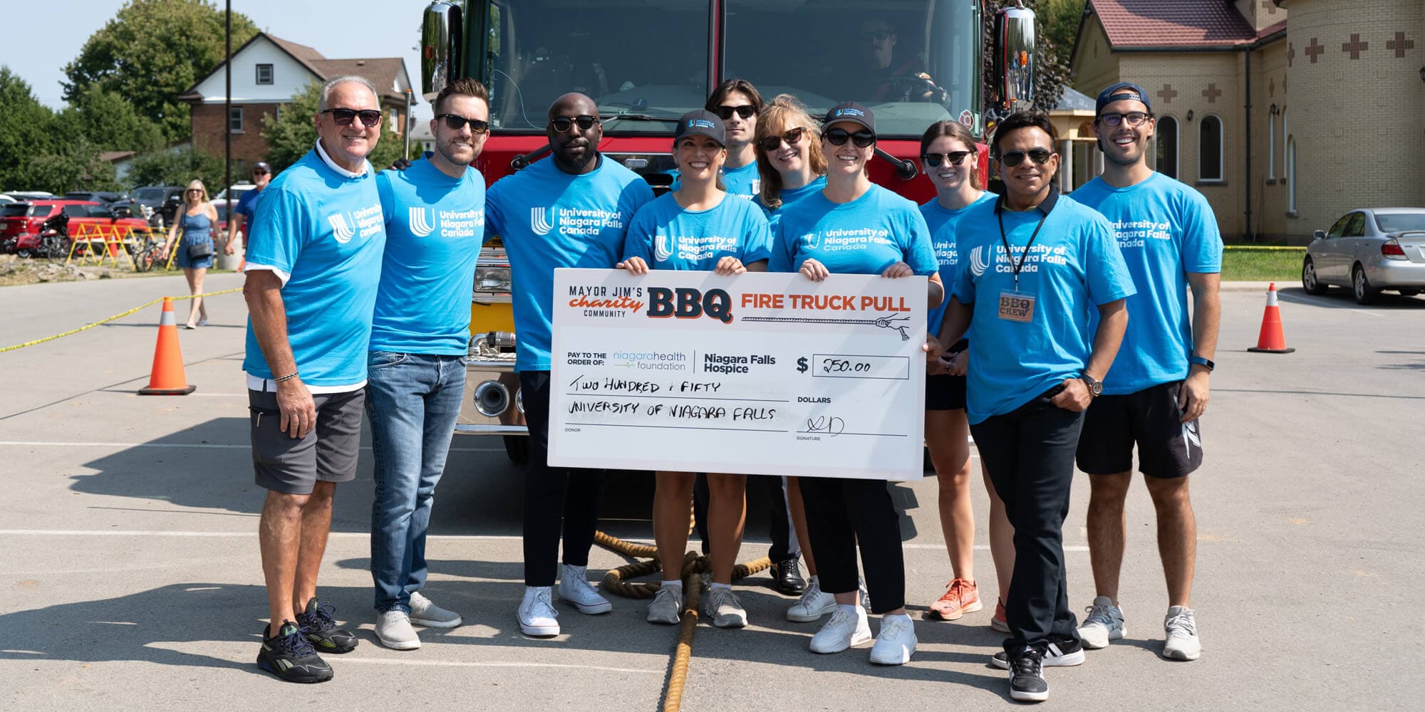 A group of individuals in blue shirts proudly holding a large check worth two hundred fifty dollars, celebrating a significant achievement together