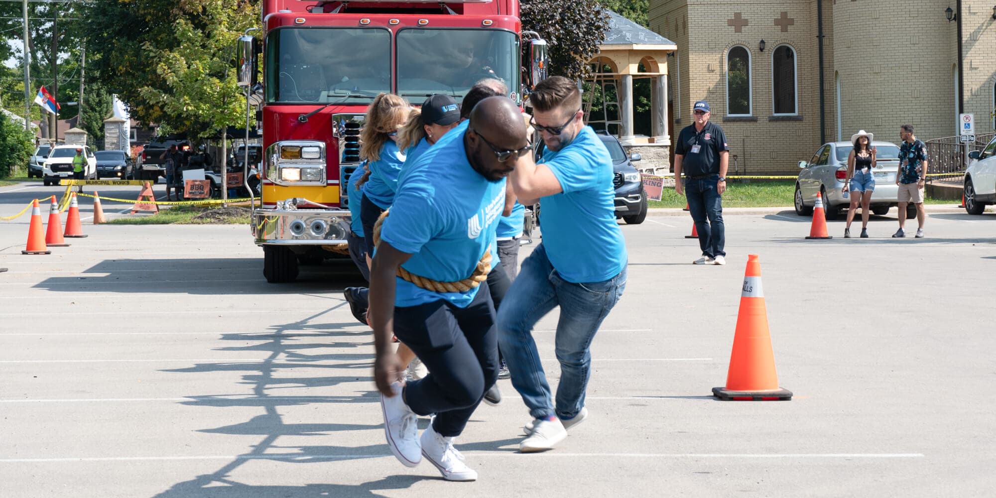 A group of individuals in blue shirts collaboratively pulling a rope tied to a firetruck, showcasing teamwork and effort in action