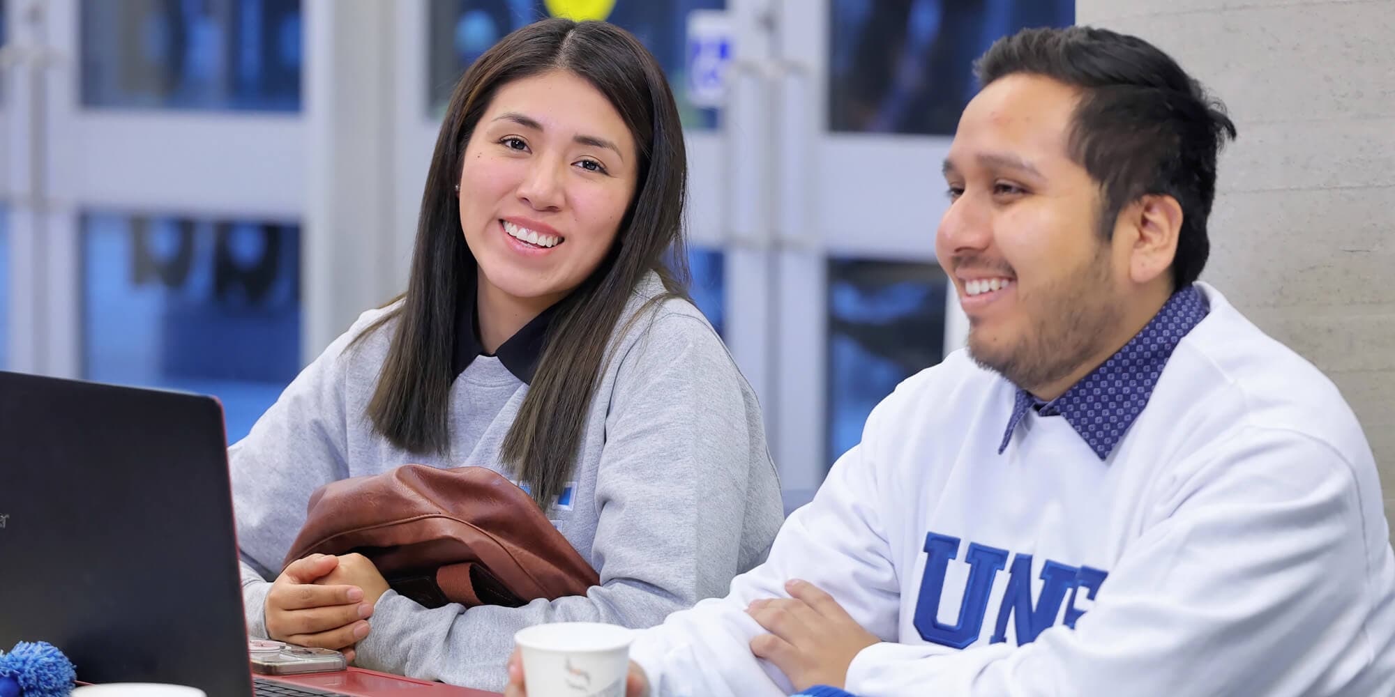 Two students collaborate at a table, each focused on their laptops, engaged in a productive study session