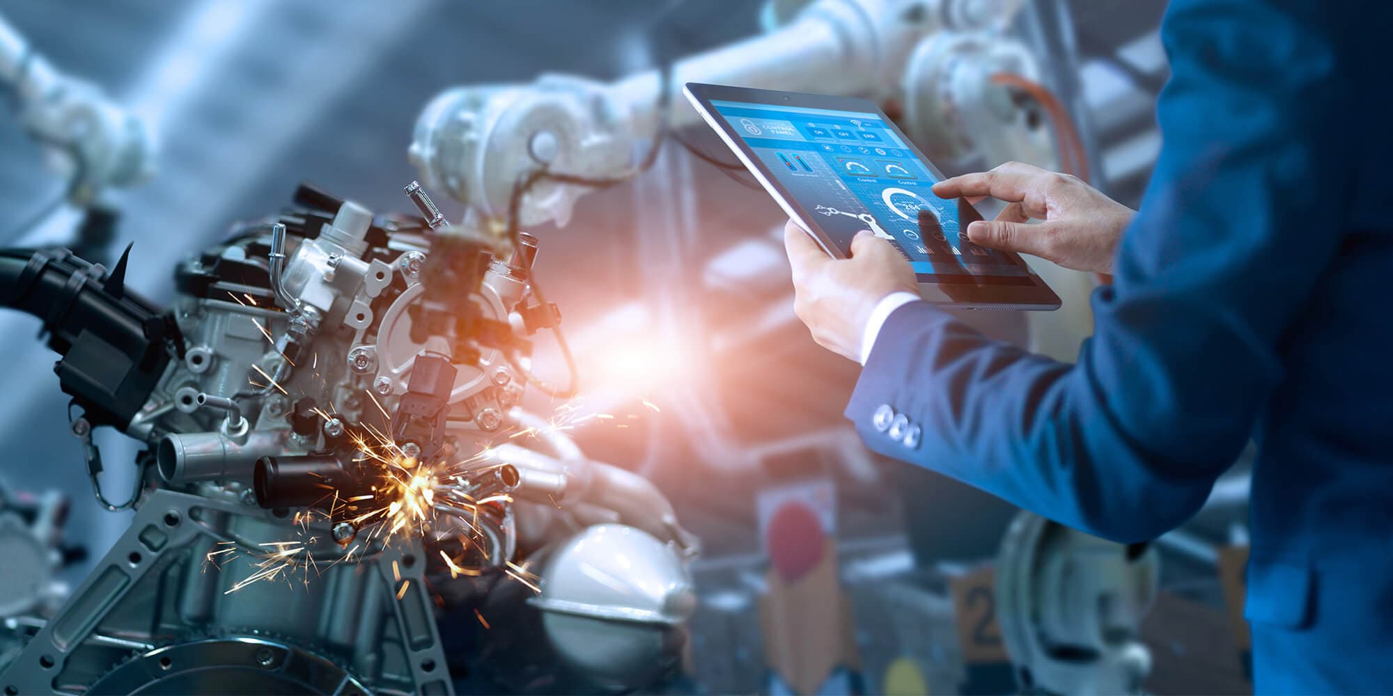 A suited man displays a tablet while standing before a futuristic manufacturing machine, showcasing technology and innovation