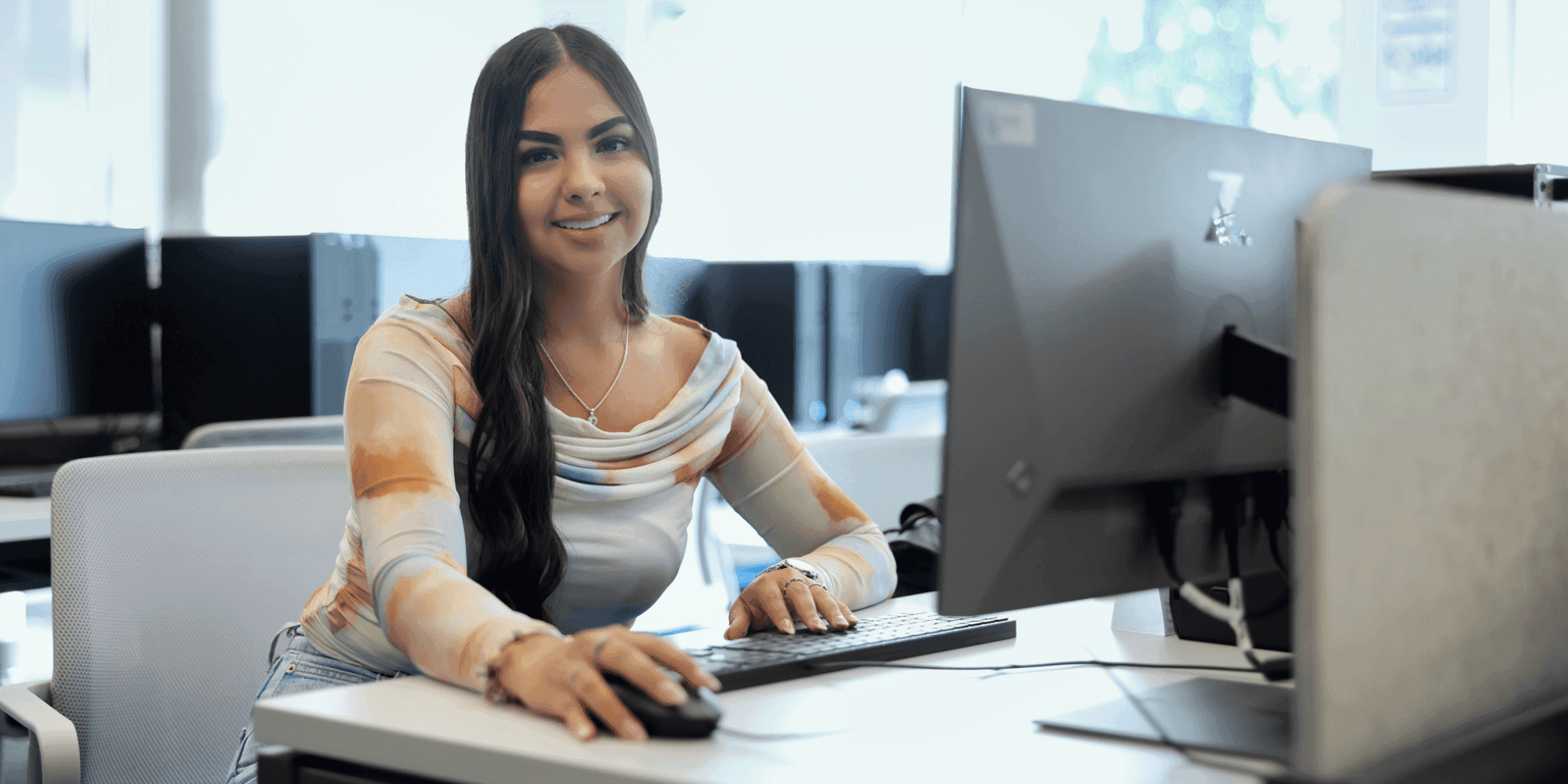 A female student sitting in front of a computer smiling at the camera