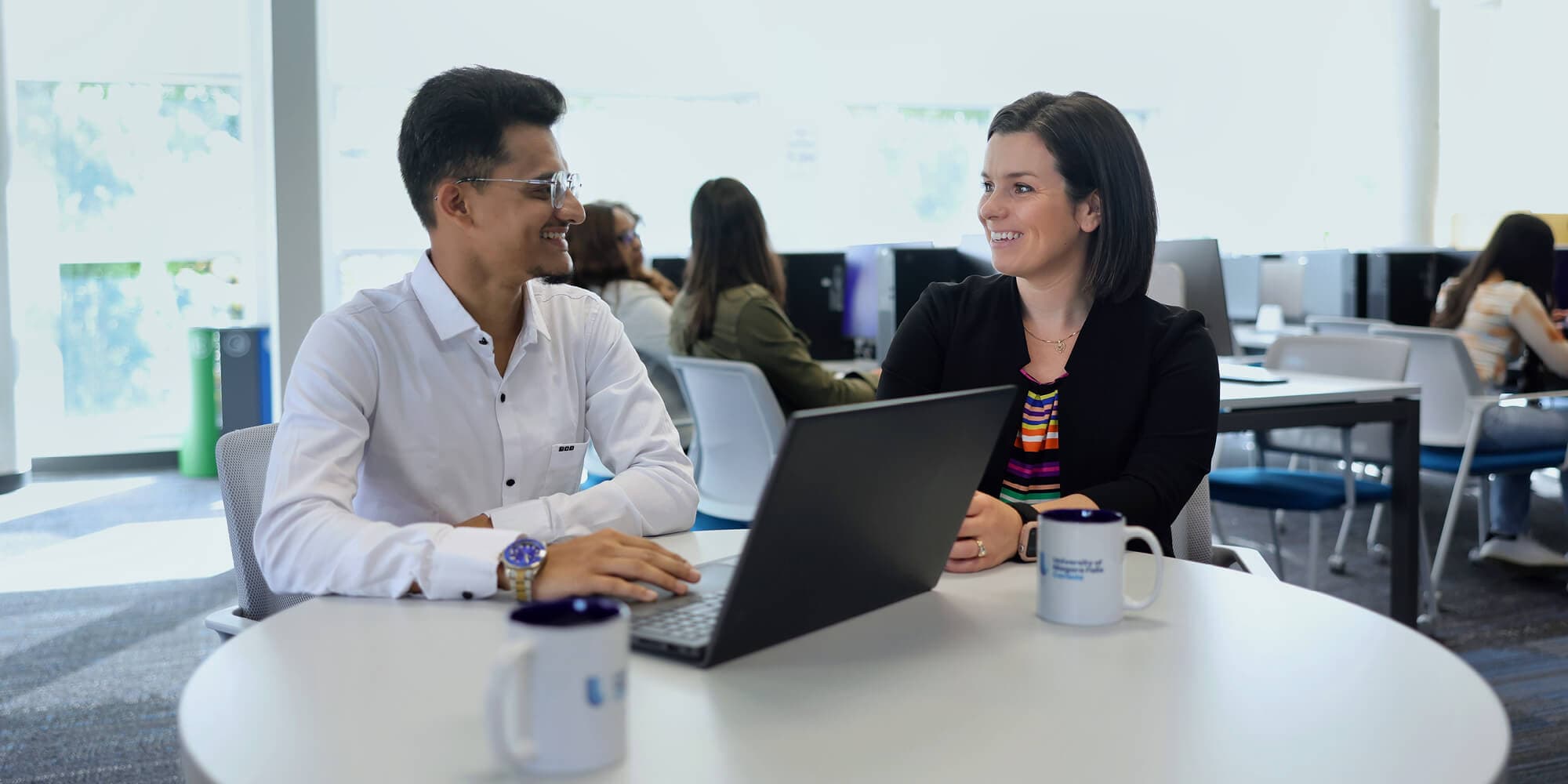 A man with a laptop talking to a woman on a table