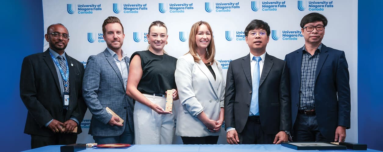 A diverse group of individuals stands together in front of a large blue banner, smiling and engaged in conversation