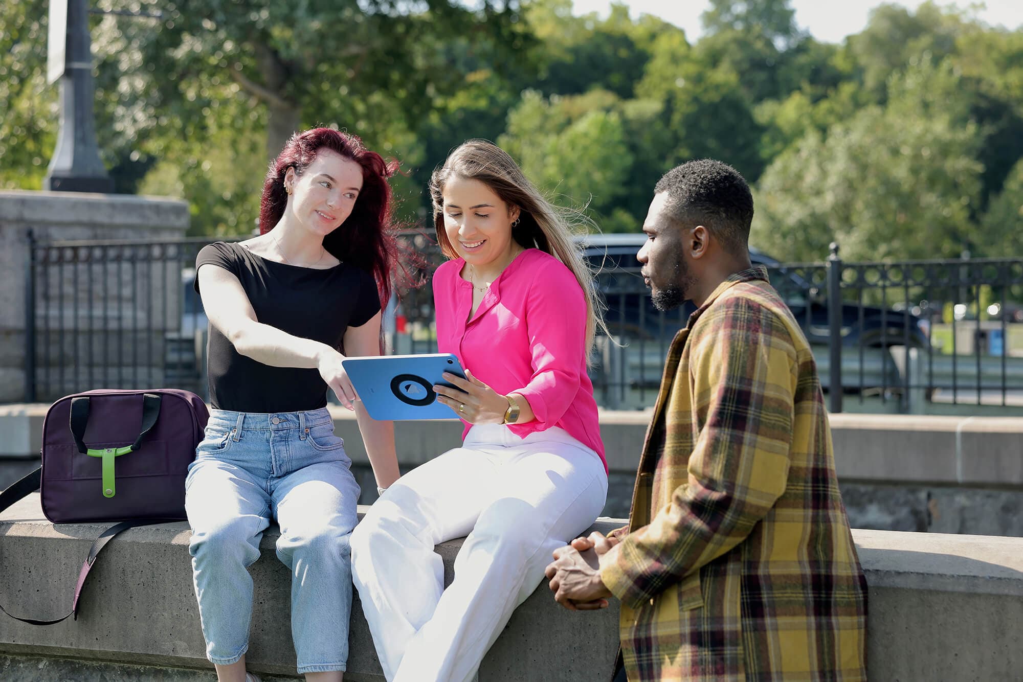Three individuals having a conversation and look at an ipad outside UNF campus