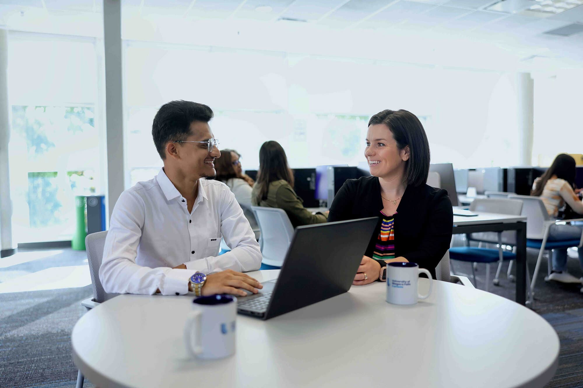 A man and a woman engaged in a cheerful discussion in front of a laptop