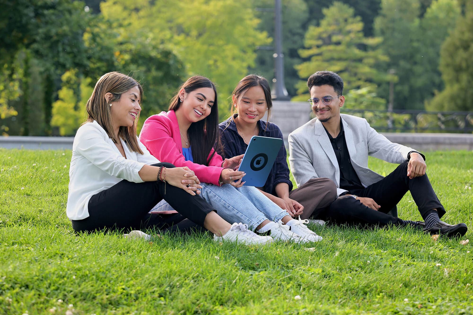 A group of diverse individuals looking at an ipad and sitting on a grass outside UNF campus