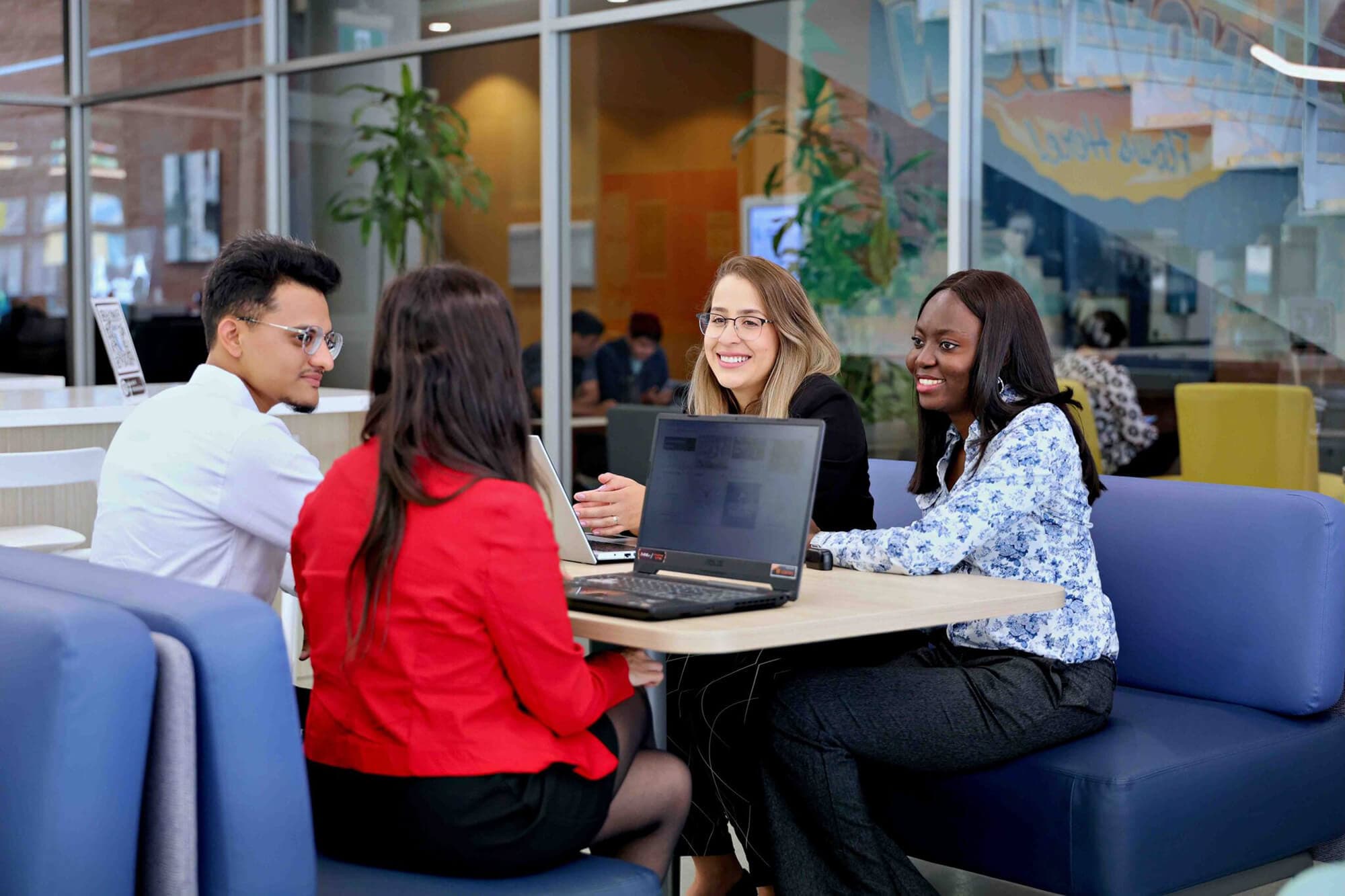 A group of diverse individuals with laptops engaged in a conversation on a comfortable learning environment