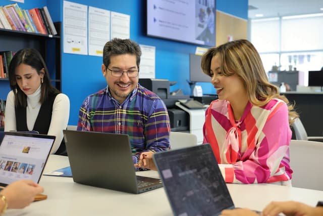 A diverse group of individuals collaborates around a table, each engaged with their laptops in a productive setting
