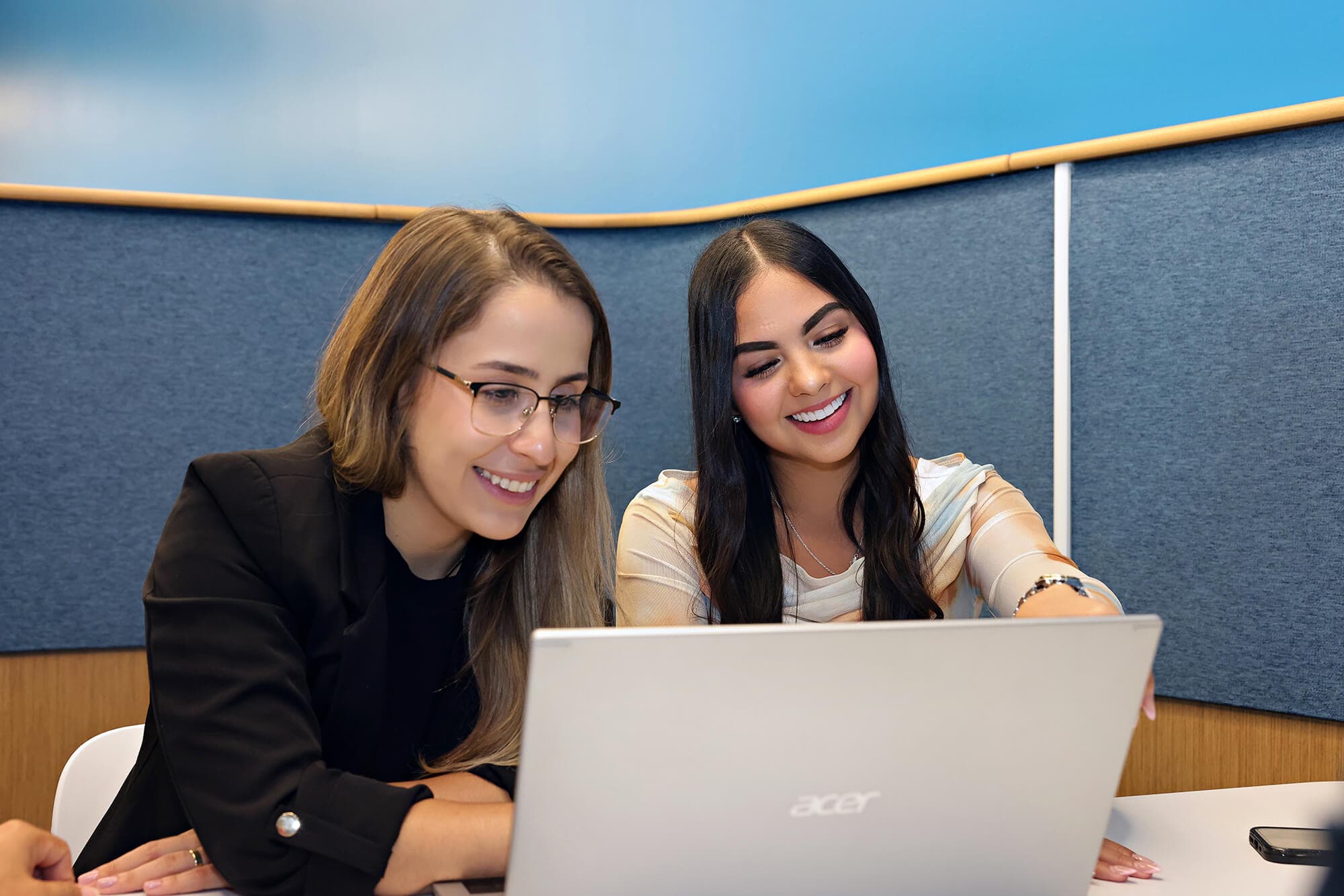 Two women smiling and looking at a laptop in front of them