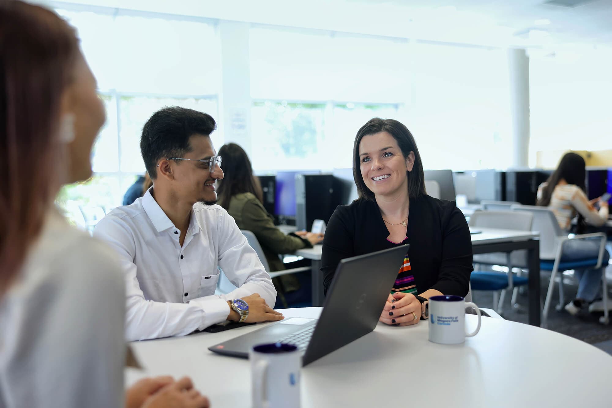 A group of individuals seated at a table, in front of a laptop, engaged in a collaborative work session