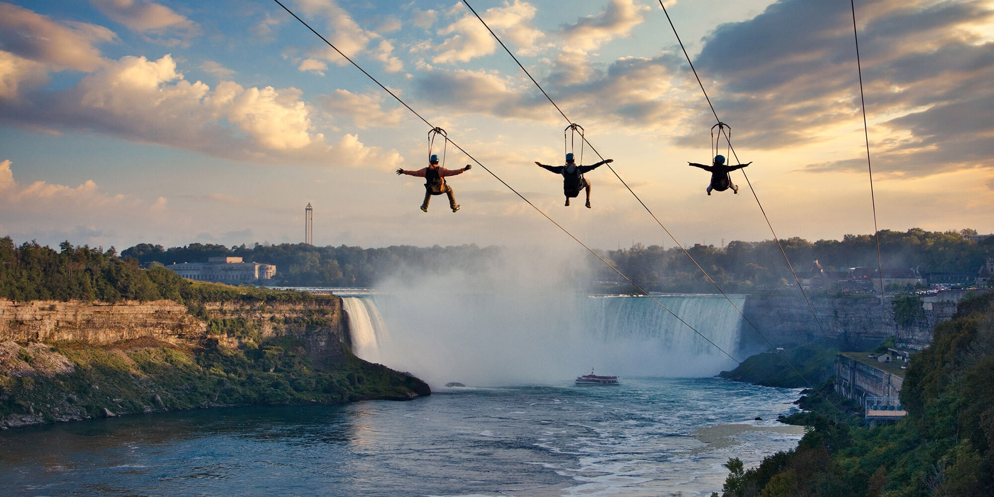 Three adventurers ride a zipline high above Niagara Falls, enjoying a stunning view of the iconic natural wonder below