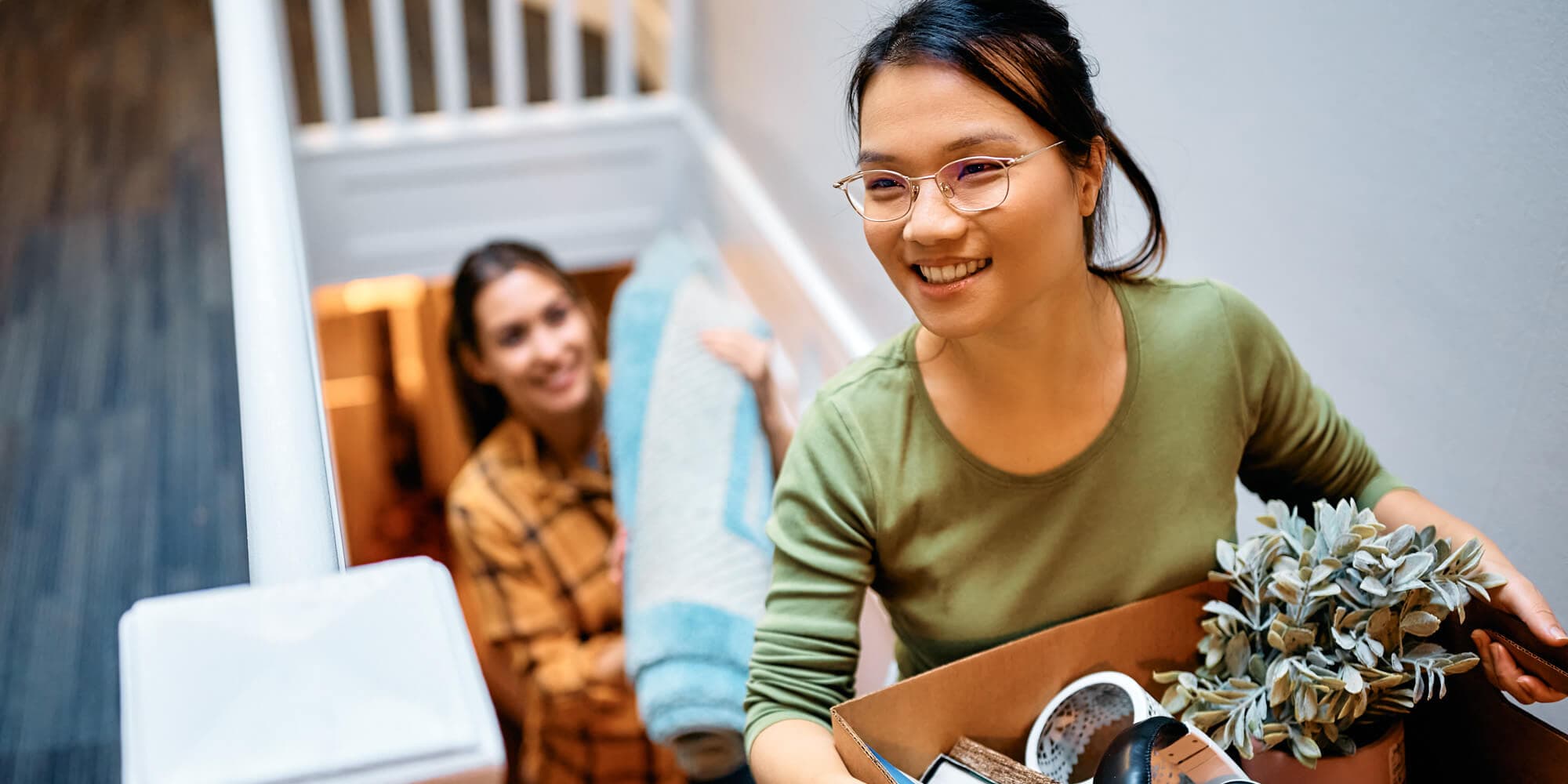 A woman holds a box in one hand with a potted plant in the other, showcasing her stylish and eco-friendly choices